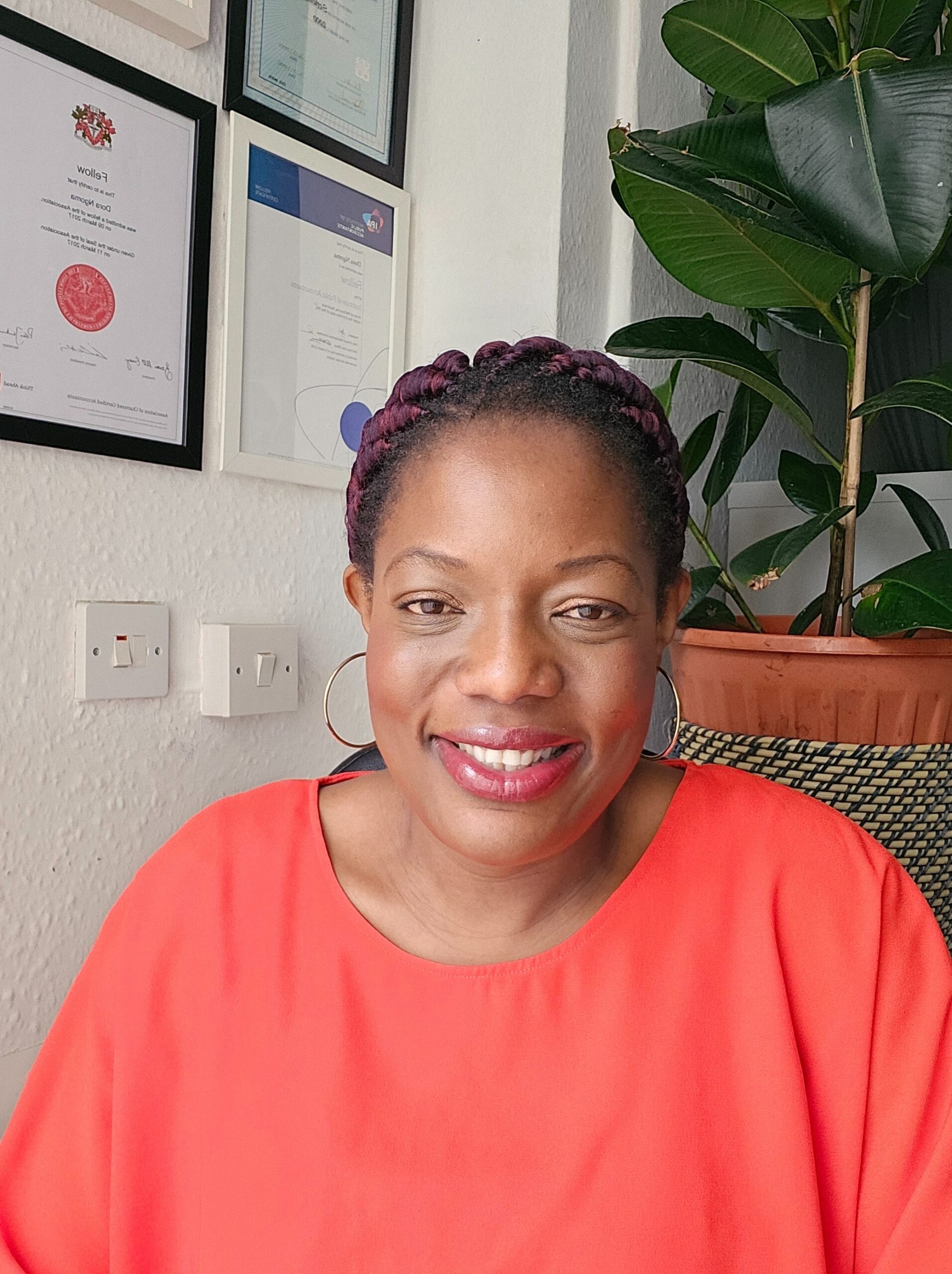 Dora Ngoma, founder of Grace Certified Accountants, smiling in her office next to framed certificates.